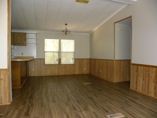 empty room featuring an inviting chandelier, wainscoting, wood finished floors, and wooden walls