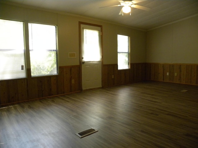 spare room with a ceiling fan, visible vents, wainscoting, wood walls, and ornamental molding