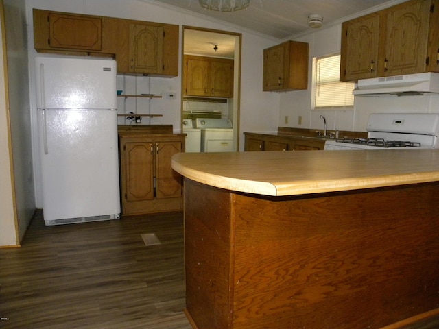 kitchen with dark wood-style flooring, white appliances, washer and clothes dryer, under cabinet range hood, and brown cabinets