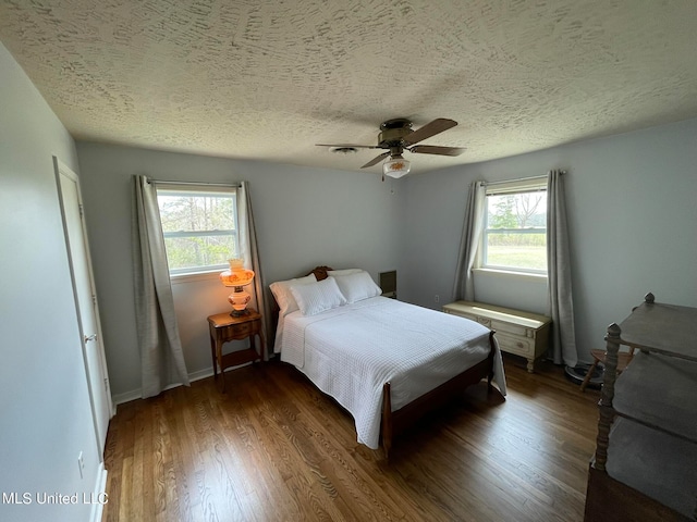 bedroom featuring dark hardwood / wood-style flooring, a textured ceiling, multiple windows, and ceiling fan