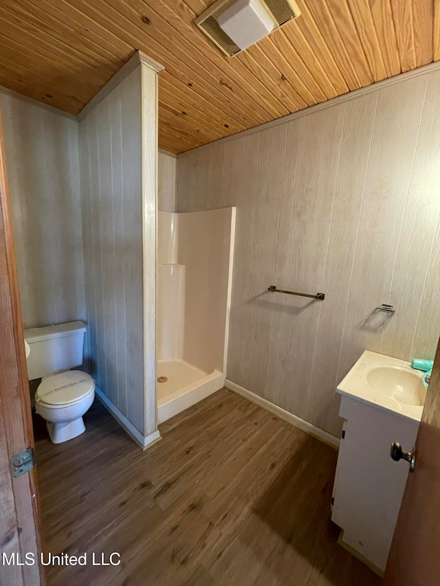 bathroom featuring toilet, hardwood / wood-style floors, walk in shower, vanity, and wood walls