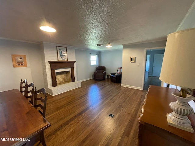 living room with dark wood-type flooring, a textured ceiling, ornamental molding, and a fireplace