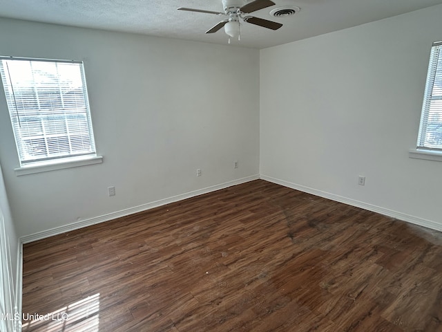 spare room featuring a wealth of natural light, visible vents, and dark wood-style flooring