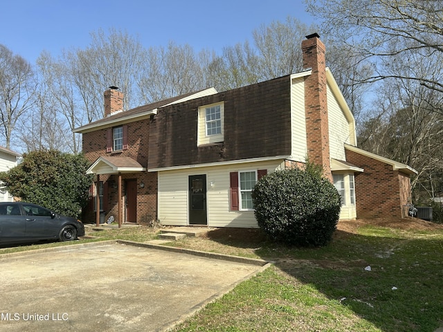 view of front of home with a front yard, central AC unit, roof with shingles, a chimney, and brick siding