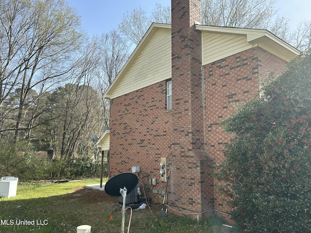 view of home's exterior with brick siding, a chimney, and a yard