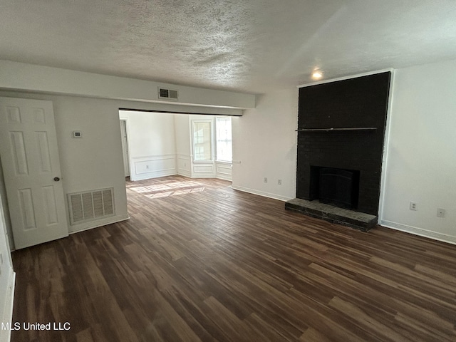 unfurnished living room featuring a brick fireplace, visible vents, dark wood-style flooring, and a textured ceiling