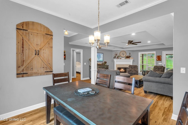 3007 Cross Point Cv, Brandon, MS 39042 - dining room featuring light wood-style floors, ceiling fan, a raised ceiling, crown molding, and a warm lit fireplace
