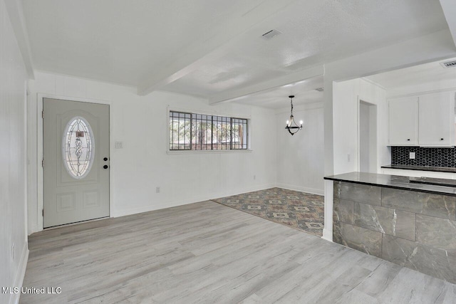 foyer entrance featuring light hardwood / wood-style flooring, beamed ceiling, and a chandelier