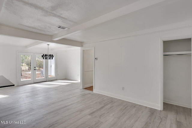 unfurnished living room featuring beamed ceiling, a textured ceiling, light wood-type flooring, and french doors