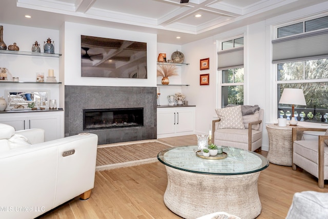 living area featuring beamed ceiling, coffered ceiling, light wood-type flooring, and a glass covered fireplace