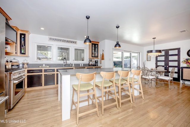 kitchen with visible vents, glass insert cabinets, high end stainless steel range, decorative light fixtures, and a center island