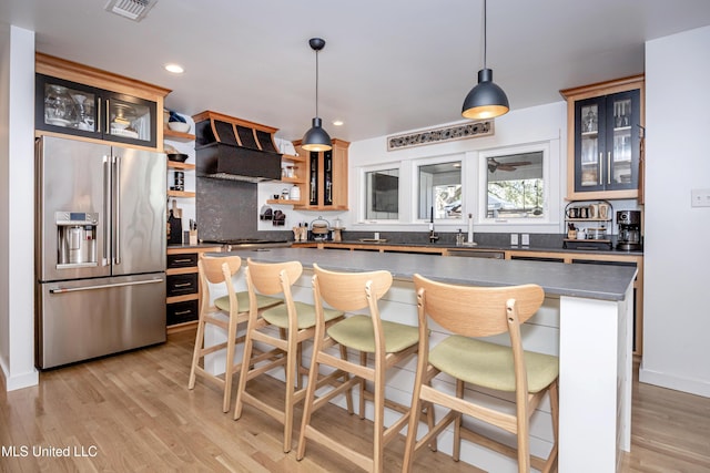 kitchen featuring glass insert cabinets, dark countertops, high quality fridge, and hanging light fixtures