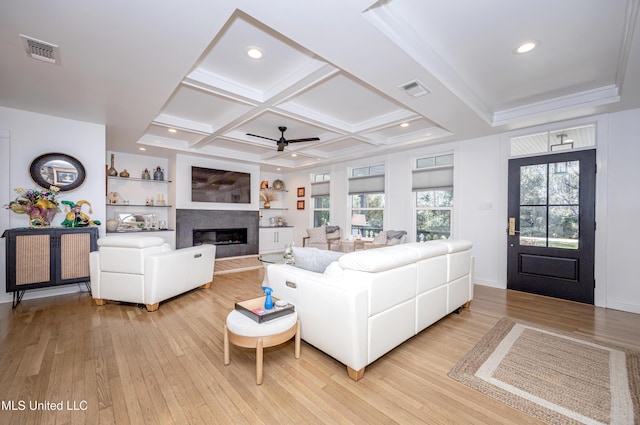 living area with coffered ceiling, light wood-type flooring, visible vents, and a glass covered fireplace