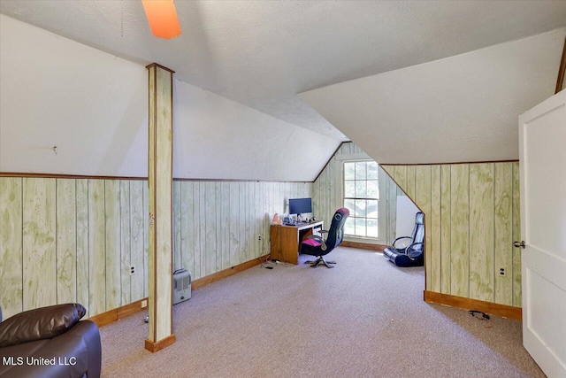 home office with light carpet, a textured ceiling, ceiling fan, lofted ceiling, and wood walls