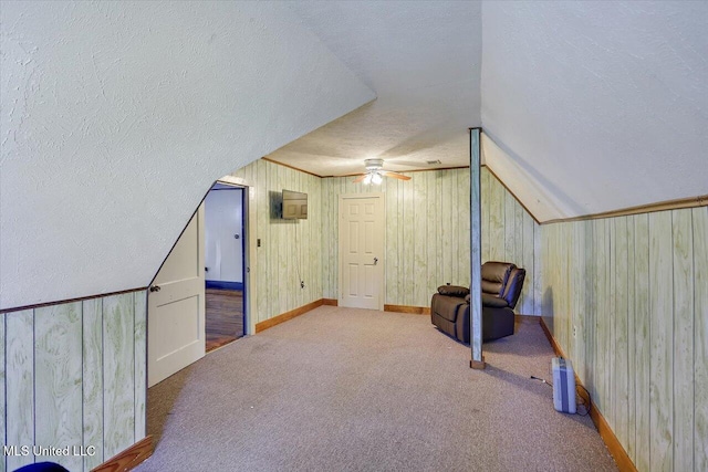 bonus room featuring ceiling fan, wood walls, carpet floors, lofted ceiling, and a textured ceiling