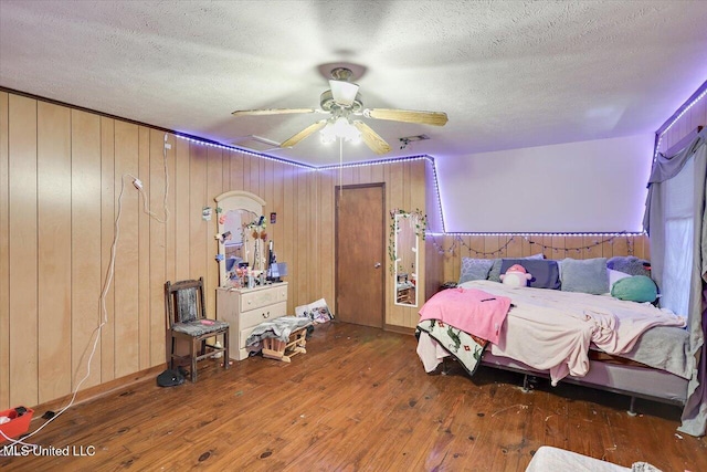 bedroom with wood walls, ceiling fan, dark hardwood / wood-style floors, and a textured ceiling