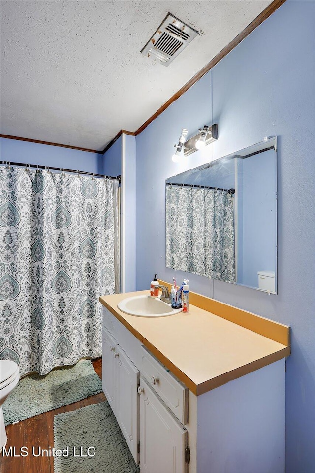 bathroom featuring hardwood / wood-style flooring, vanity, a textured ceiling, and ornamental molding