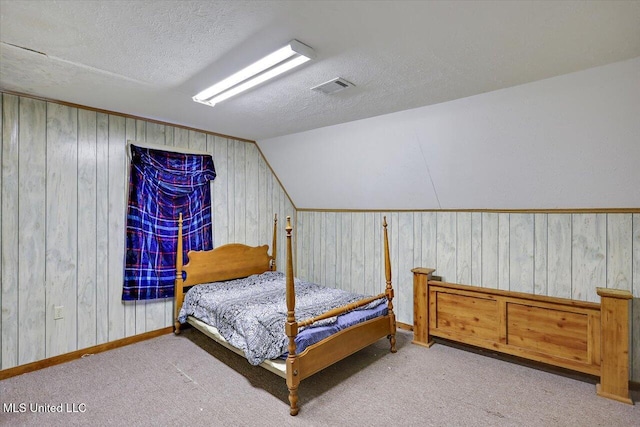 bedroom with a textured ceiling, wood walls, lofted ceiling, and light carpet