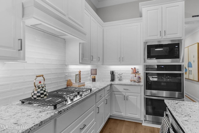 kitchen featuring light stone countertops, stainless steel appliances, dark hardwood / wood-style flooring, backsplash, and white cabinets