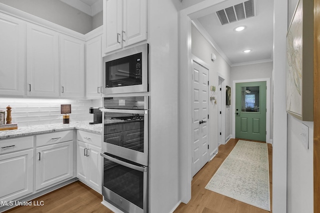 kitchen featuring built in microwave, stainless steel double oven, decorative backsplash, white cabinets, and light wood-type flooring