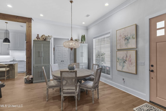 dining room featuring light hardwood / wood-style flooring, crown molding, and a notable chandelier