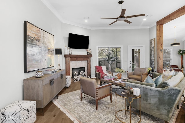 living room featuring a tiled fireplace, ceiling fan, ornamental molding, and hardwood / wood-style flooring