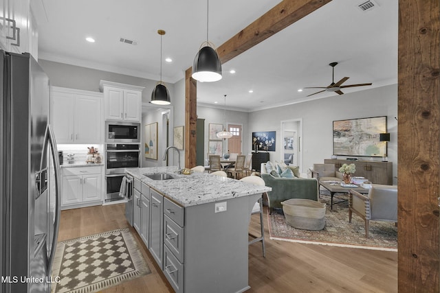 kitchen featuring light stone countertops, stainless steel appliances, a kitchen island with sink, sink, and white cabinetry