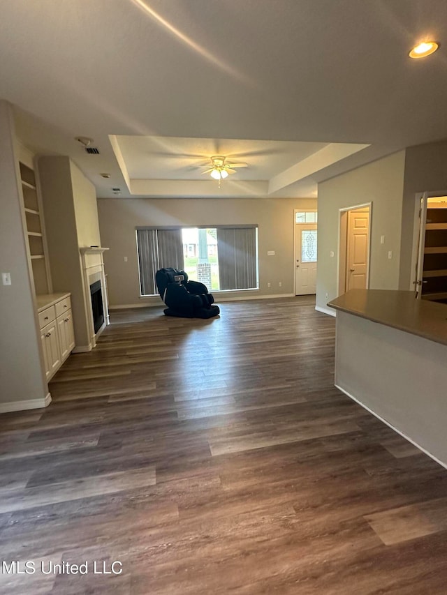 unfurnished living room with a raised ceiling, ceiling fan, and dark hardwood / wood-style flooring