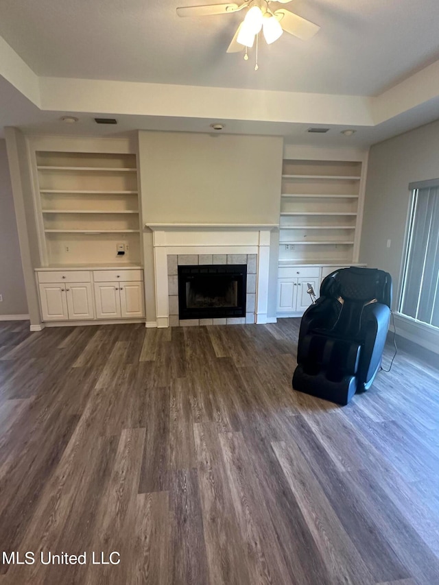 unfurnished living room with built in shelves, a tiled fireplace, dark hardwood / wood-style floors, and ceiling fan