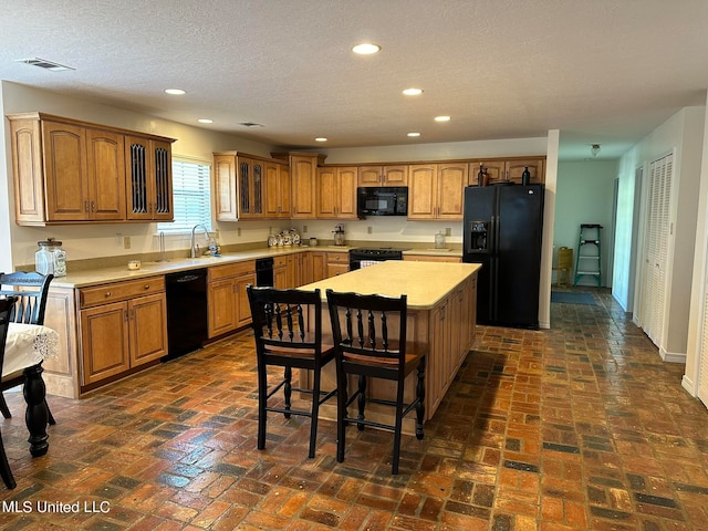 kitchen featuring a breakfast bar, a textured ceiling, black appliances, sink, and a center island