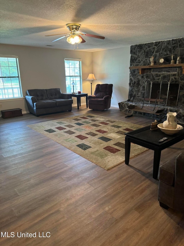 living room with a stone fireplace, a textured ceiling, wood-type flooring, and plenty of natural light