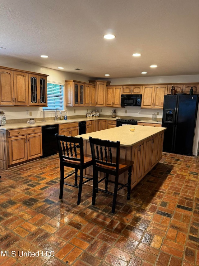 kitchen featuring a kitchen island, a textured ceiling, a kitchen bar, black appliances, and sink