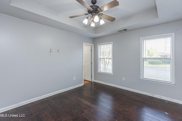 unfurnished room with a raised ceiling, ceiling fan, dark hardwood / wood-style flooring, and a healthy amount of sunlight