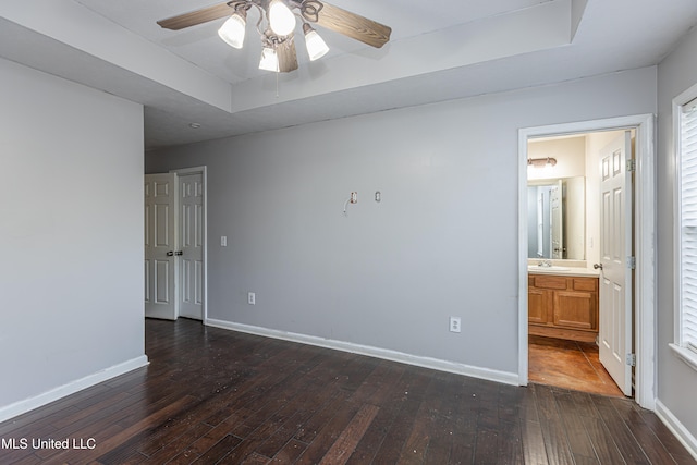 unfurnished bedroom featuring a tray ceiling, ensuite bathroom, ceiling fan, and dark hardwood / wood-style floors