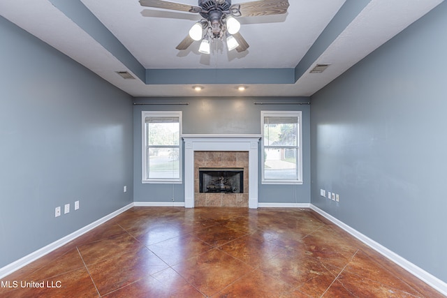 unfurnished living room featuring a tray ceiling, ceiling fan, and a tiled fireplace