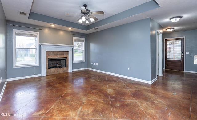 unfurnished living room with ceiling fan, a raised ceiling, a wealth of natural light, and a tiled fireplace