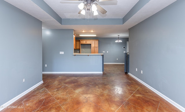 unfurnished living room featuring a tray ceiling and ceiling fan with notable chandelier