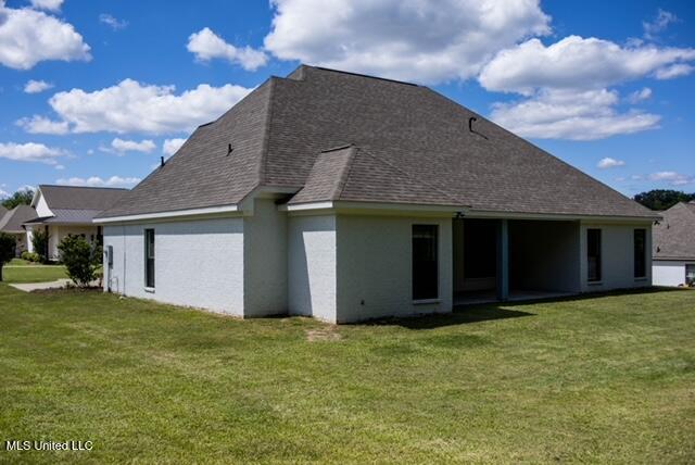 back of house featuring a lawn, roof with shingles, and stucco siding