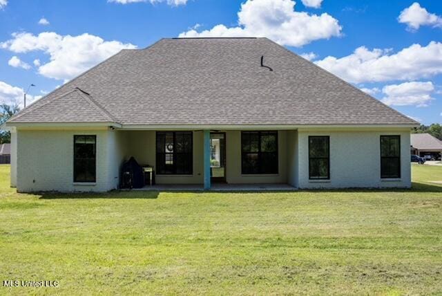 rear view of property featuring a lawn, a patio, stucco siding, and roof with shingles