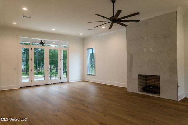 unfurnished living room with french doors, a tiled fireplace, dark wood-type flooring, ornamental molding, and ceiling fan