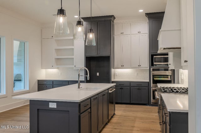 kitchen featuring sink, stainless steel appliances, custom exhaust hood, light hardwood / wood-style flooring, and a center island with sink