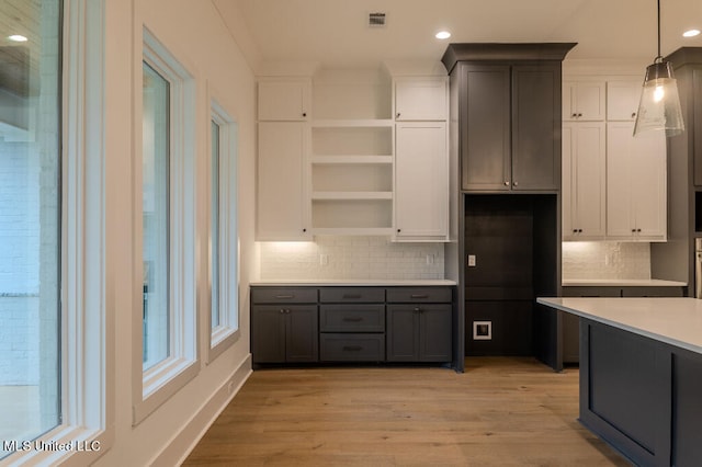 kitchen with white cabinets, hanging light fixtures, light hardwood / wood-style floors, and tasteful backsplash