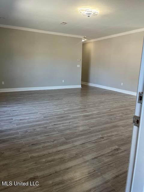 empty room featuring dark wood-style floors, ornamental molding, and baseboards