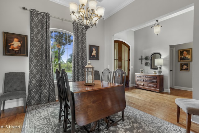 dining room with hardwood / wood-style flooring, ornamental molding, a high ceiling, and an inviting chandelier