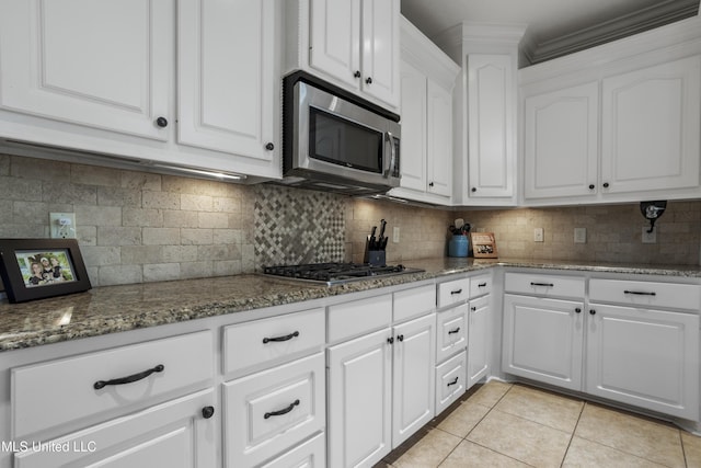 kitchen featuring light tile patterned floors, white cabinets, appliances with stainless steel finishes, stone counters, and backsplash