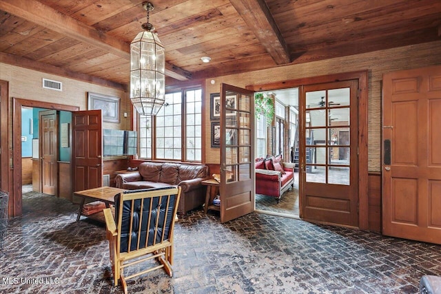 sitting room with beam ceiling, french doors, a notable chandelier, wood walls, and wood ceiling