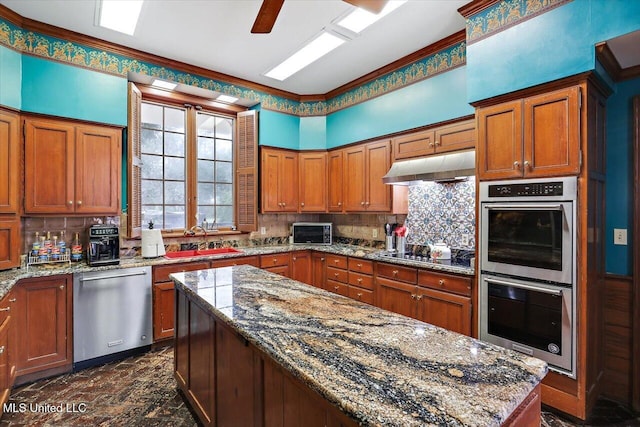 kitchen featuring backsplash, sink, light stone countertops, a kitchen island, and stainless steel appliances