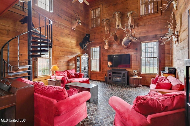 living room with ceiling fan, wood walls, a towering ceiling, and a fireplace