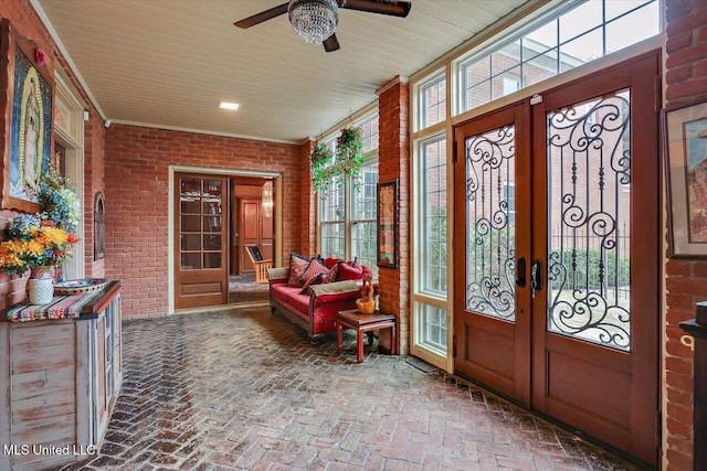 foyer with french doors, crown molding, ceiling fan, a wealth of natural light, and brick wall