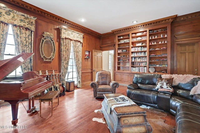 living room featuring a healthy amount of sunlight, crown molding, wooden walls, and hardwood / wood-style floors